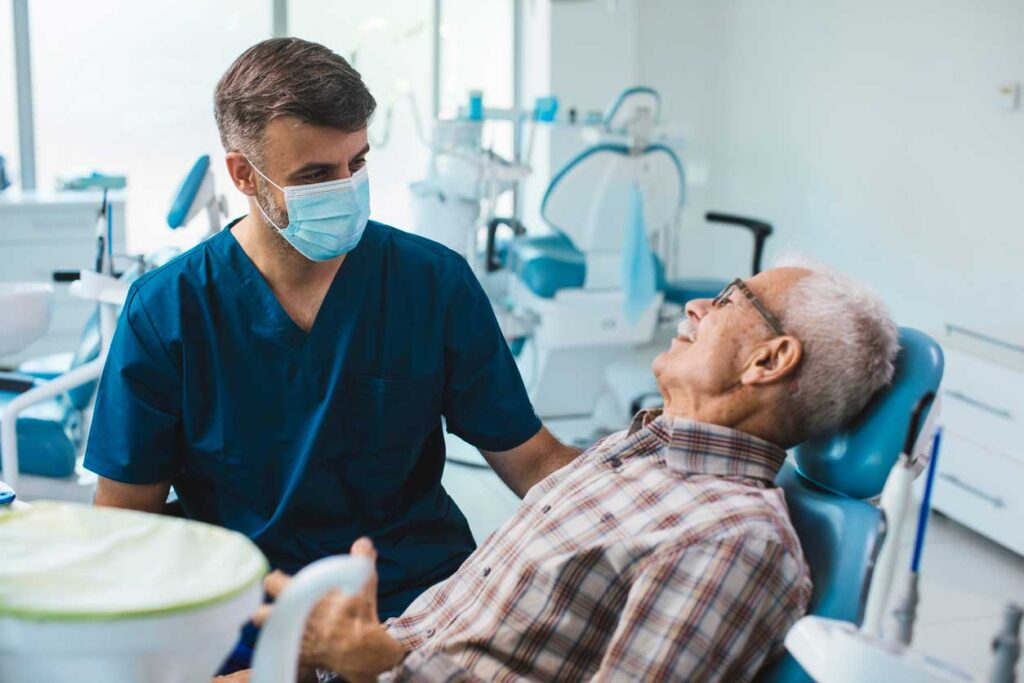 Male dentist consulting with an older male patient in a dental exam room.
